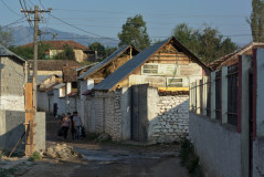 Bild: Dorf Cetushë - Dorfstraße mit Stromleitung, Häusern, Bach und Fußgängern